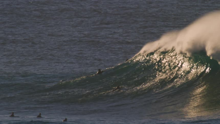 A large wave breaks over people on surfboards