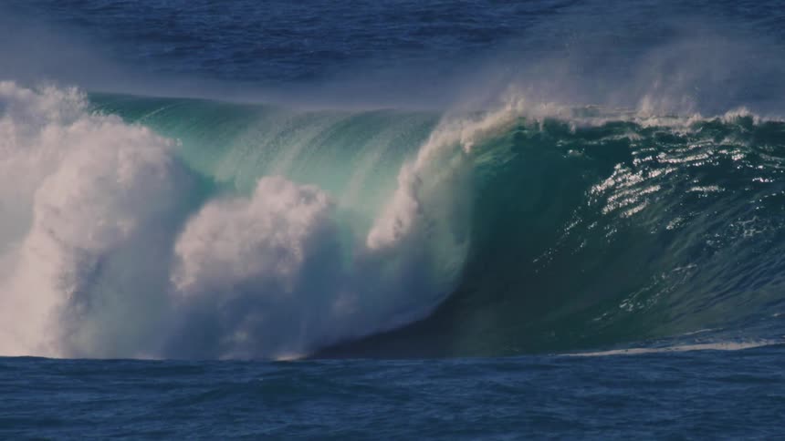 Large tubular wave breaking in the ocean with surfers and people on jet skis