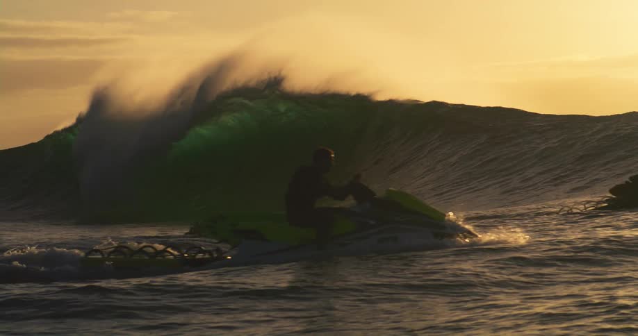 People in boats and on a jet ski watch a large wave break near them in the ocean