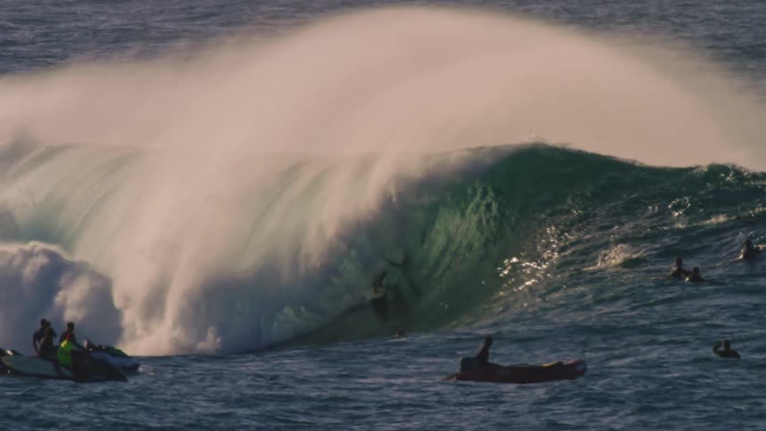 A surfer is paddling to catch a breaking wave and he is getting barreled then coming out of the wave