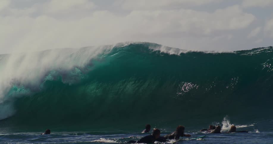 Group of surfers paddling against a tubular wave