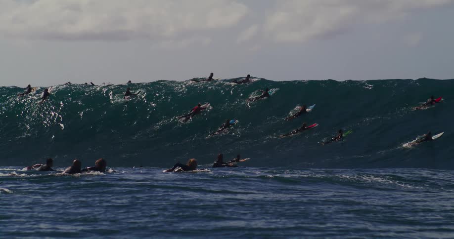 Several surfers are paddling up to a wave that is almost breaking on top of them
