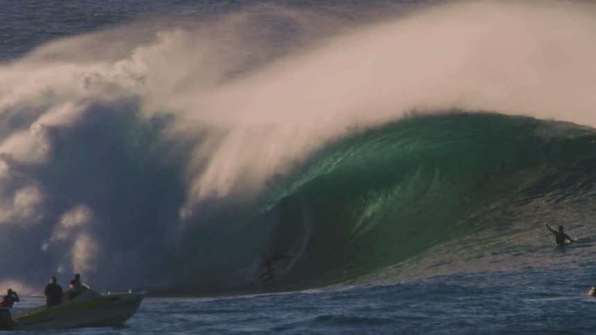 Surfer riding a tubular wave accompanied by other people watching from the ocean