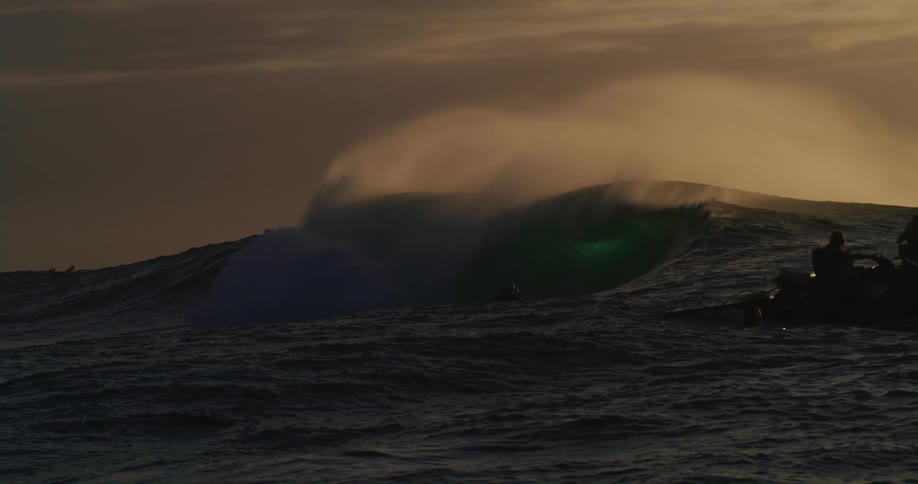 Surfers with surfboards and people on jet skis in an ocean with strong waves