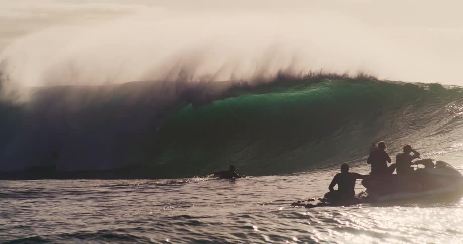 People on a jet ski and surf board watch a wave break