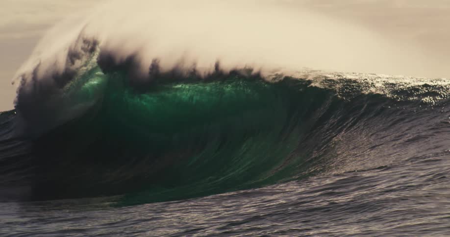 Silhouette of a person with a camera in the ocean next to a tubular wave