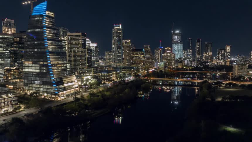 City skyline lit up at night with skyscrapers reflected in the river and a busy bridge in the center