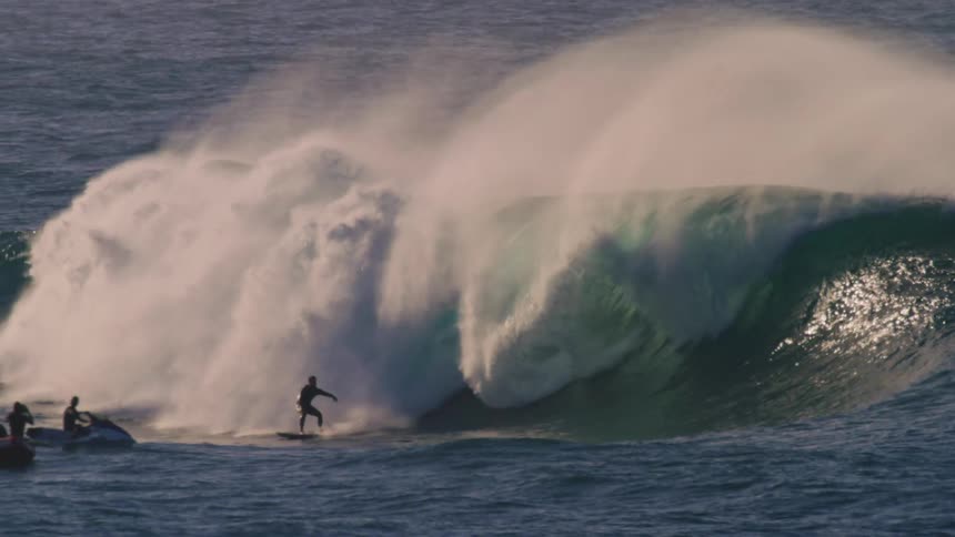 Surfer riding a big wave and other people watching from the sea