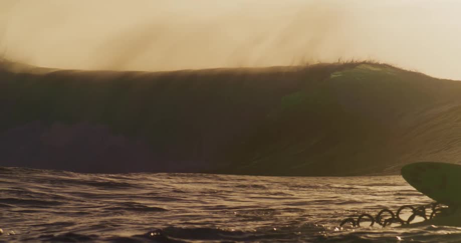 A huge wave breaking and making a splash of water and to a nearby surfer paddling