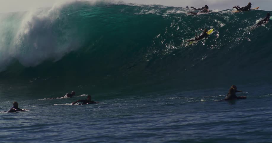 Some surfers are paddling towards a breaking wave and some of them are falling into it