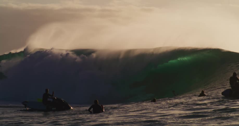 A surfer is riding a breaking wave next to some other people who are standing on their surfboards and there are some jet skis