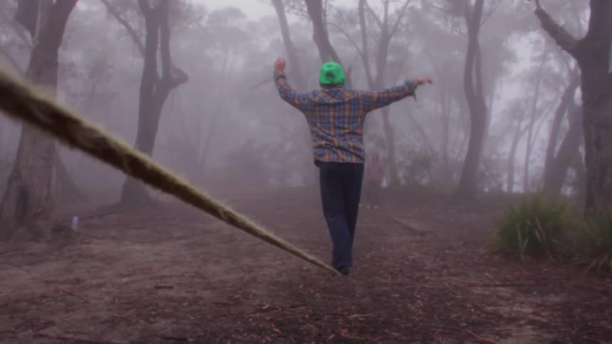 A man balances on a rope in the woods