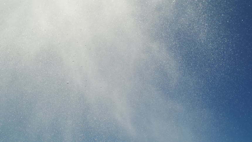 Various water particles falling into a body of water on a day with blue sky