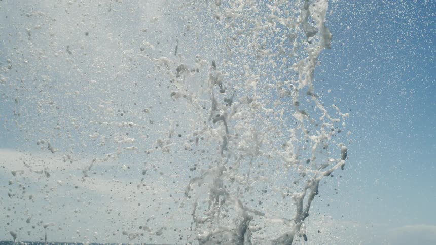 Jet of steam and water expelled by a whale forming a white cloud against the blue sky and ocean