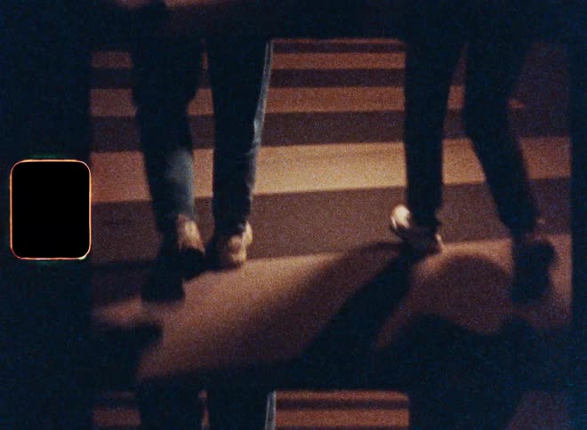 Two people walk at night on bricks then on a crosswalk