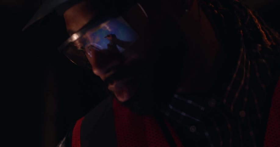 Close up of an African-American male construction worker who is intently focused on a blueprint, marking details with a square pencil, as the camera pans to reveal he is  on a construction site and wearing safety gear.