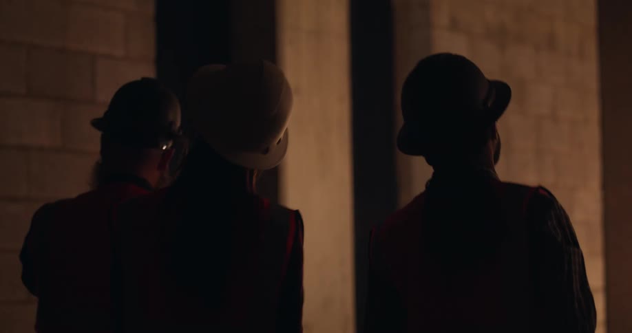 Three engineers wearing hard hats and reflective vests analyze a tablet while observing the structure of a construction site at night.