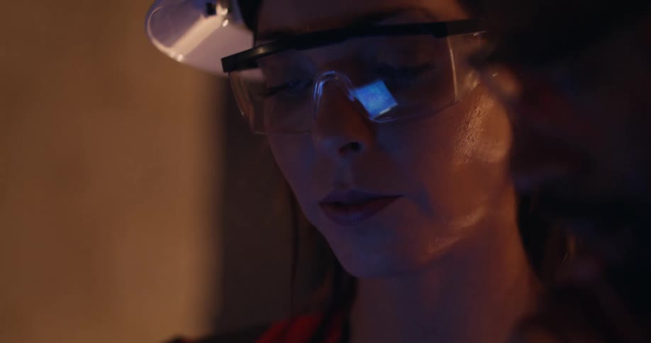 Close up of a female engineer with safety gear and hard hat on, talking to a male colleague next to her as they discuss what's on the screen that's reflected in her safety glasses.