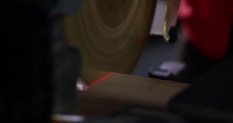 View from behind the rotating blade and panning to the side of a miter saw being used to cut a piece of 2x4 wood.