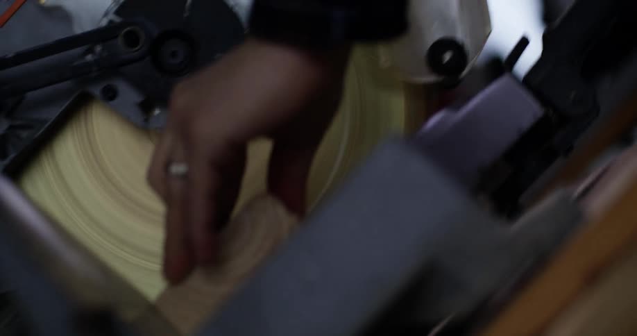 View of the circulating blade and handle of a miter saw being pulled down to make the cut on a piece of wood.