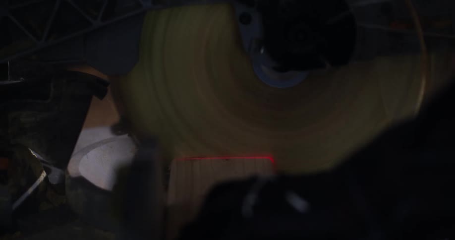 Close up of the rotating blade of a miter saw being pulled down to cut a piece of two-by-four wood.