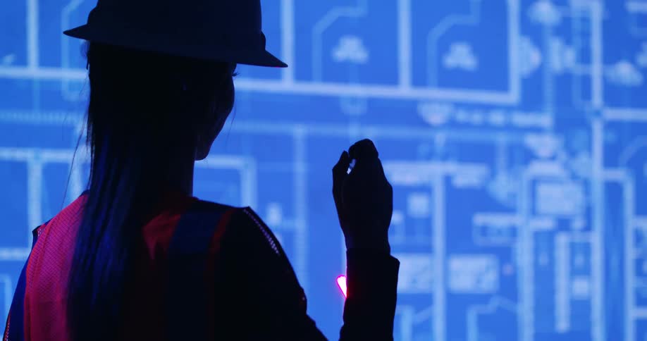 Silhouette of a female civil engineer wearing a hard hat and safety vest and using a laser pointer to highlight details on a blueprint being projected on screen.