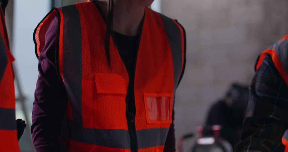 Close of up of the hands and then faces of a female and two male engineers deliberating over blueprints in an active indoor construction zone.