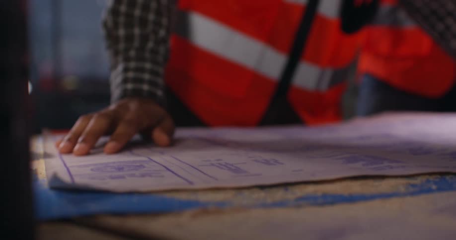 Construction workers unroll and consult project blueprints during an onsite meeting.
