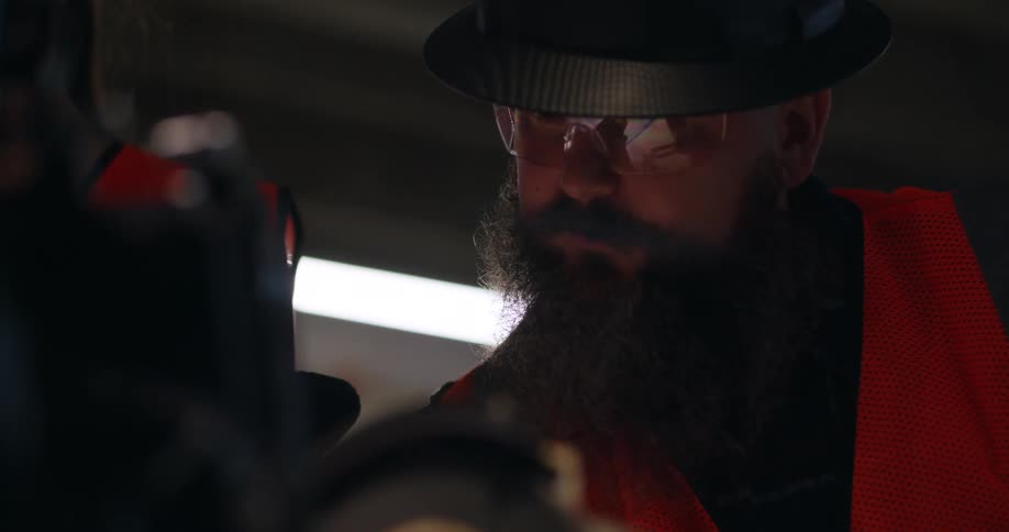 Close up of a bearded white male construction foreman, wearing safety gear and a hard hat, looking down at project plans and discussing with others in a building site.