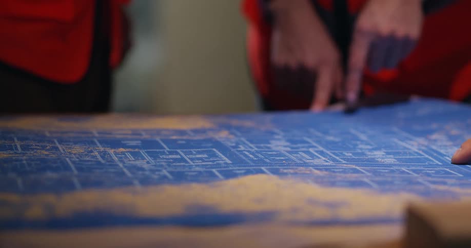 Hands of three engineers pointing and interacting over project blueprints on a table.