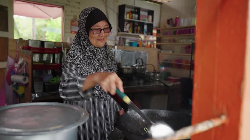Woman wearing a scarf and glasses cooks in a wok inside a simple and organized kitchen