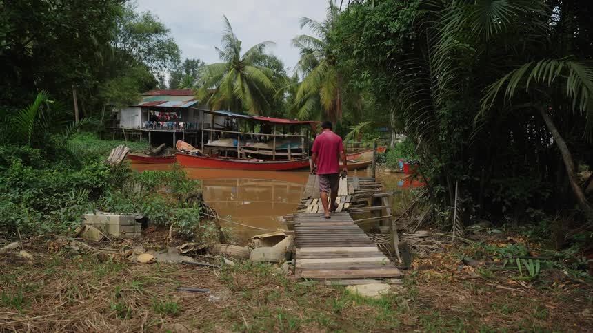 Man crossing a wooden bridge over a polluted river in a community in the middle of a rainforest