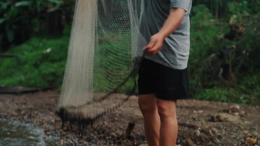 Man adjusting a fishing net on the bank of a river