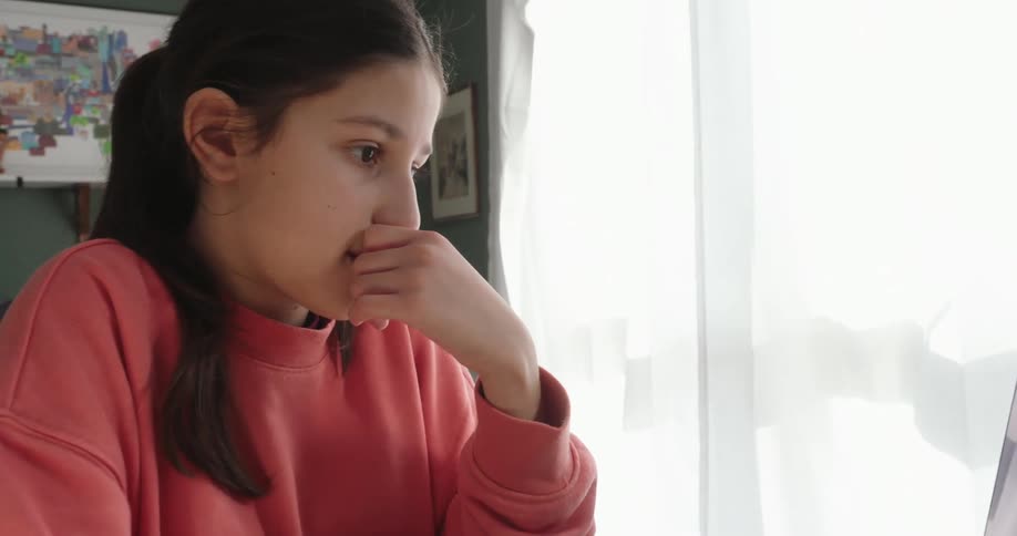 A girl types on a laptop then sits back and puts her hand at her face