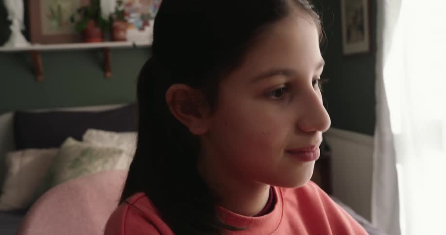 A teen girl wearing a pink blouse is smiling while typing on the computer