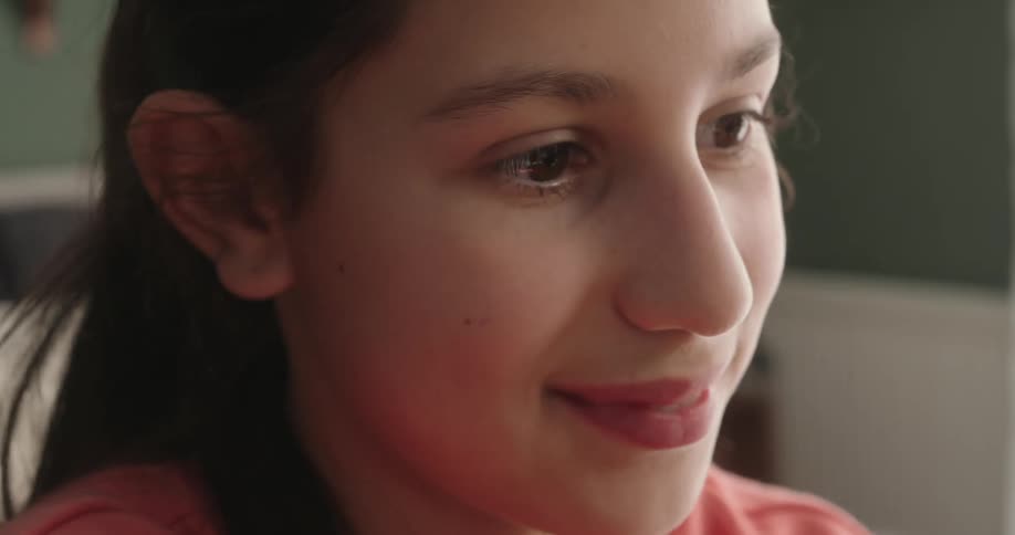 Close up of the face of a girl wearing a pink sweatshirt in a room near a window