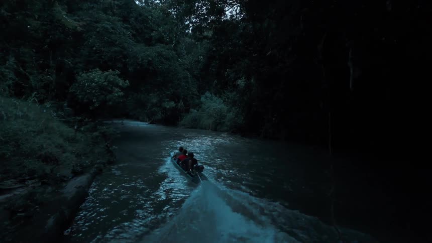 Three people are in a small boat with a motor sailing on a river among lots of vegetation