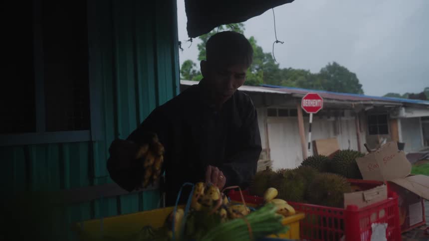 Man putting a bunch of bananas in a box with other fruits around it