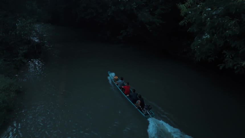 Men on a boat make their way down a river through a jungle