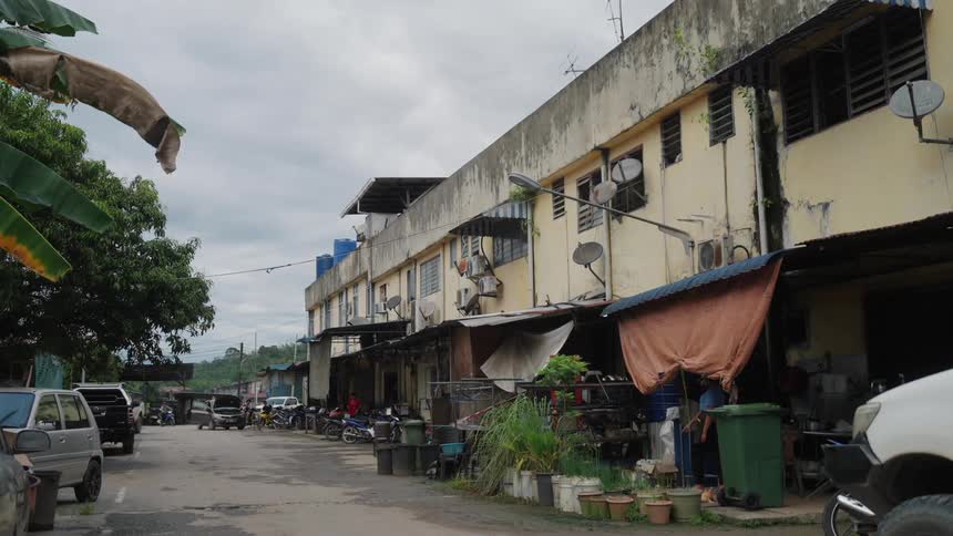 A narrow street lined with weathered multistory buildings featuring exposed utility lines and a variety of parked vehicles under an overcast sky