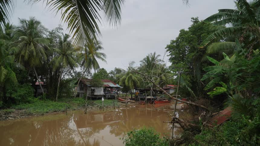 Boats float in the muddy river water near houses built on stilts
