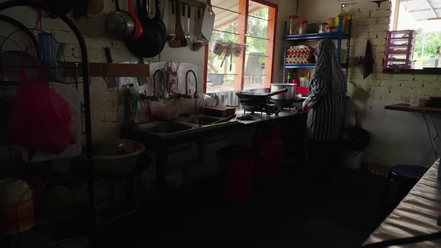 A woman stands at a stove in a house kitchen and prepares food