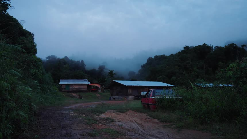 Small rural village surrounded by dense vegetation and mountains covered in mist at dawn