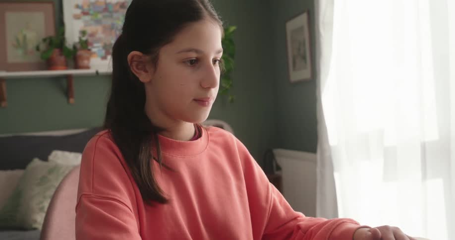 Girl sitting at a table in a room typing on a laptop