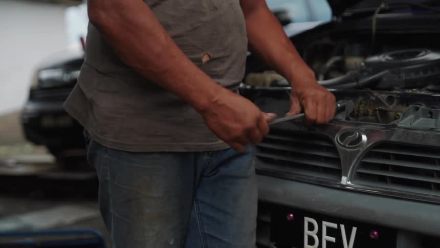 A person is working on a car engine with the hood open using a tool to make adjustments