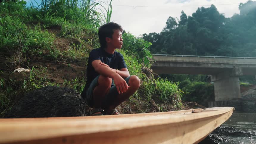 Young man crouching next to a wooden canoe in a river