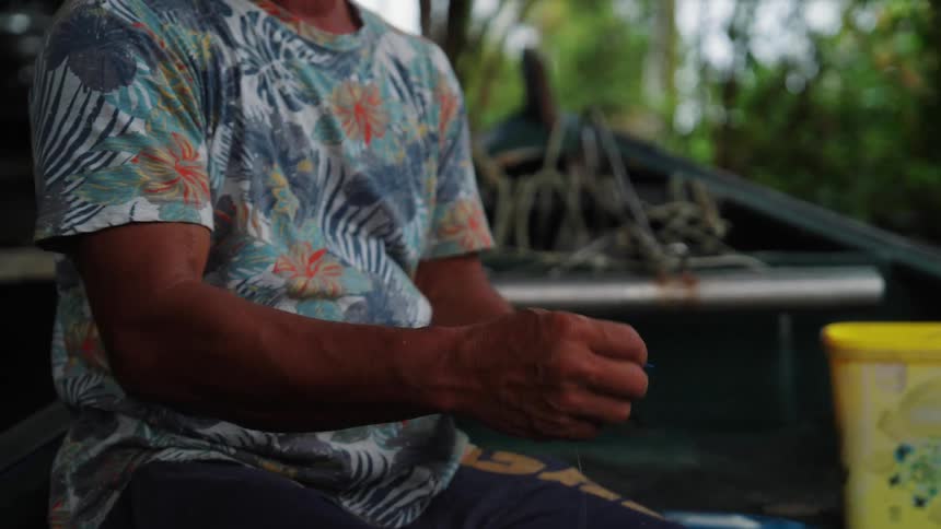 A fisherman sitting in a boat on a river removing fishing line off of a spool
