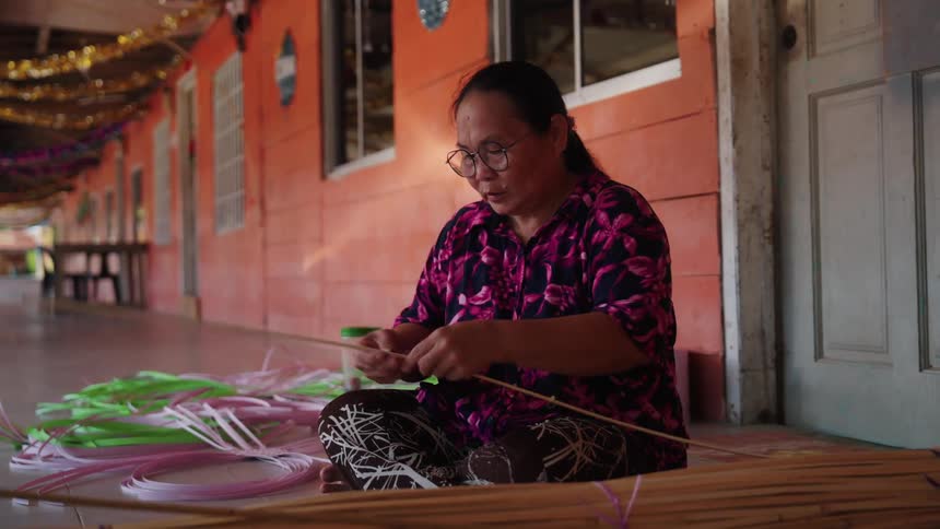 A woman sits outside and prepares to weave