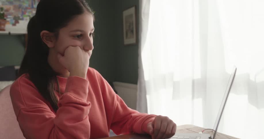Young teenage girl sitting at a table interacting with a laptop