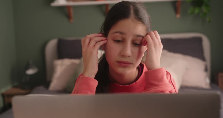 Girl with thoughtful facial expression interacting in front of a laptop